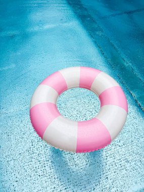 Mavi bir açık havuzda pembe ve beyaz çizgili yüzme ringi. Havuz başı atmosferi. Pembe şamandıra. Su partisi.