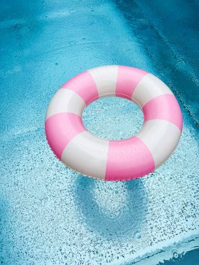 Mavi bir açık havuzda pembe ve beyaz çizgili yüzme ringi. Havuz başı atmosferi. Pembe şamandıra. Su partisi.