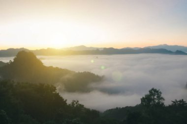 Doğal sis ve dağların arka planı bulanıklaşıyor, sisli dalgalar ılık renkler ve parlak güneş ışığı. Noel arkaplanı gökyüzü güneşli turuncu ışık desenleri, bulutlarda soyut aydınlatma akşamı bulanık.