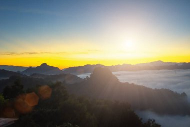 Doğal sis ve dağların arka planı bulanıklaşıyor, sisli dalgalar ılık renkler ve parlak güneş ışığı. Noel arkaplanı gökyüzü güneşli turuncu ışık desenleri, bulutlarda soyut aydınlatma akşamı bulanık.