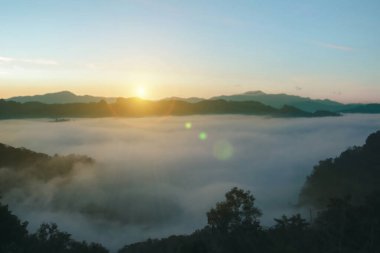 Doğal sis ve dağların arka planı bulanıklaşıyor, sisli dalgalar ılık renkler ve parlak güneş ışığı. Noel arkaplanı gökyüzü güneşli turuncu ışık desenleri, bulutlarda soyut aydınlatma akşamı bulanık.