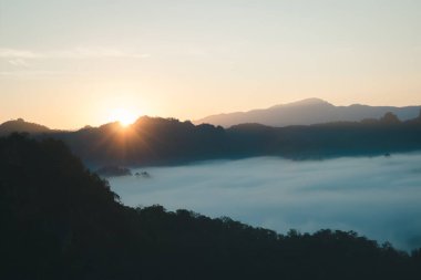 Doğal sis ve dağların arka planı bulanıklaşıyor, sisli dalgalar ılık renkler ve parlak güneş ışığı. Noel arkaplanı gökyüzü güneşli turuncu ışık desenleri, bulutlarda soyut aydınlatma akşamı bulanık.