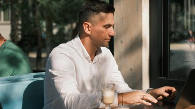 Kafedeki yetişkin iş adamı bilgisayarının monitörüne bakıyor.