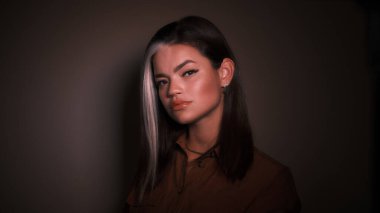 Karanlık arka planda bir kız kameraya bakıyor.