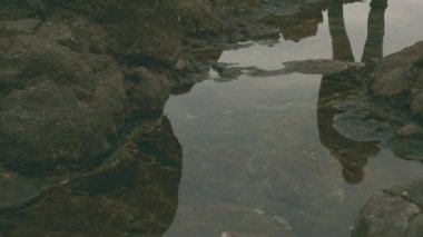 Bir turist taştan bir sahilde durur ve sırt çantasını çıkarır.
