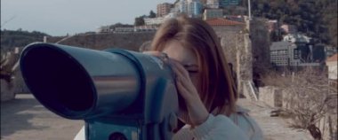 The girl on the observation deck closed one eye and looks through a spyglass