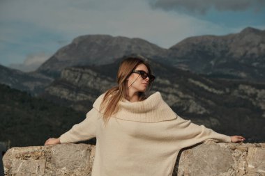 The girl put her hands on the stone wall and looks to the left
