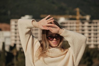 The girl covers her face from the sun with her palms and looks at the camera