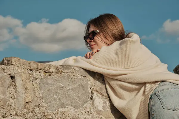 The girl leaned against a stone wall and looks ahead