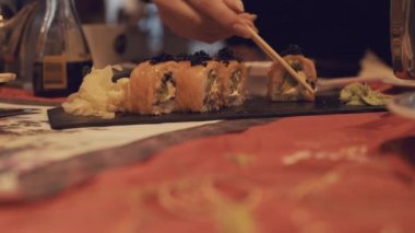 A girl takes sushi, dips it in soy sauce, and places it on a sushi tray