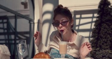 Kahve bardağını masadan kaldırmadan kamışla kahve içen yetişkin bir kız.