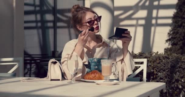 一个在夏季咖啡馆里的成年女孩用软刷把粉末涂在脸上 — 图库视频影像