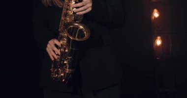 Siyah arka planda saksafon çalan genç bir kız. Yakın plan. Arka planda birkaç ampul var. Sinematik görünüm