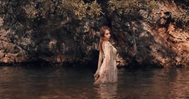 一个腰深的小女孩走近一棵树 举起她的手 触摸着它的叶子 在背景中 可以在岩石上看到水面上的闪光 Boho 湿看风格 电影观 — 图库视频影像