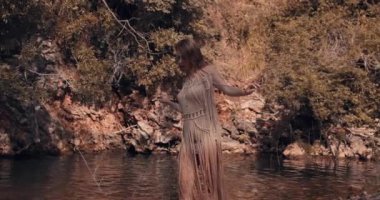 Genç bir kız küçük bir gölün kıyısında yürüyor. Arka planda kayalar ve ağaçlar görülebilir. Boho. Sinematik görünüm