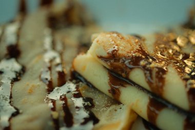 Çikolata soslu bir yığın krep. Lezzetli ve hoşgörülü bir tatlı için sos kreplerin üzerine serpilmiş..