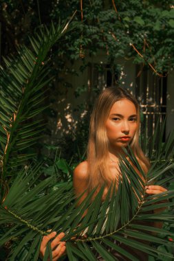 Bir kadın bir ağacın önünde yapraklarla poz veriyor. O kırmızı bir gömlek giyiyor ve elinde bir yaprak tutuyor. Görüntünün doğal ve organik bir havası var.