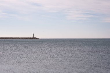 Kayalık bir kıyı şeridinde bir deniz feneri var. Su sakin ve gökyüzü bulutlu. Sahnede görünen tek şey deniz feneri.