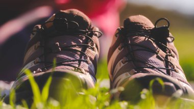 Çimlerin üzerinde iki ayakkabı var, biri kahverengi ve diğeri bronzlaşmış. Çimler yeşil ve ayakkabılar yandan görünür.