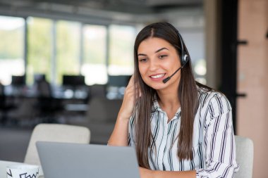 Esmer kadın dizüstü bilgisayarından arıyor kulaklık takıyor gülümsüyor ve el sallayarak web kamerasıyla iletişim kuruyor evde masada oturuyor. İnternet ve Uzaktan İletişim