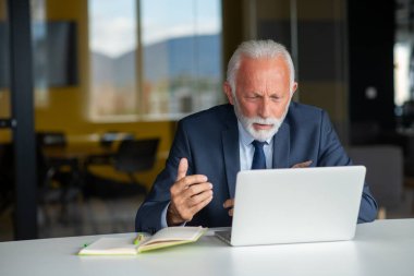 Evde dizüstü bilgisayarıyla rahat işyerinde oturan yakışıklı, gülümseyen, sosyal medyada arkadaşlarıyla sohbet eden emekli bir erkek.