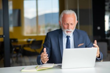 Evde dizüstü bilgisayarıyla rahat işyerinde oturan yakışıklı, gülümseyen, sosyal medyada arkadaşlarıyla sohbet eden emekli bir erkek.