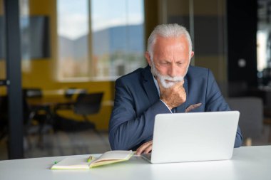 Evde dizüstü bilgisayarıyla rahat işyerinde oturan yakışıklı, gülümseyen, sosyal medyada arkadaşlarıyla sohbet eden emekli bir erkek.
