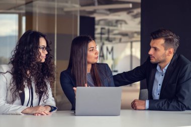 İş ekibi dizüstü bilgisayar kullanarak proje üzerinde işbirliği yapıyor. Güncel ofis ortamında sıradan iş arkadaşları birlikte çalışıyor. Takım çalışması konsepti
