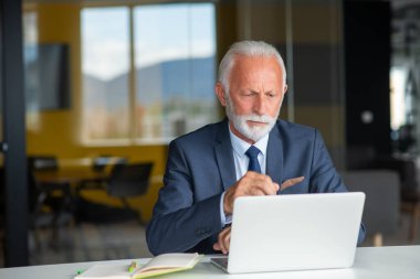 Evde dizüstü bilgisayarıyla rahat işyerinde oturan yakışıklı, gülümseyen, sosyal medyada arkadaşlarıyla sohbet eden emekli bir erkek.