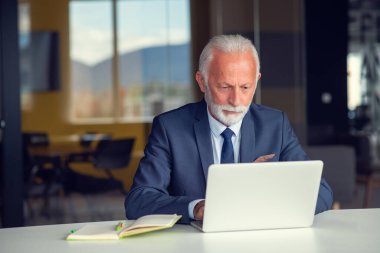 Evde dizüstü bilgisayarıyla rahat işyerinde oturan yakışıklı, gülümseyen, sosyal medyada arkadaşlarıyla sohbet eden emekli bir erkek.