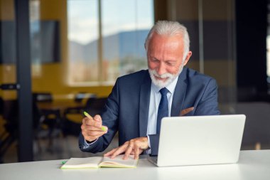 Evde dizüstü bilgisayarıyla rahat işyerinde oturan yakışıklı, gülümseyen, sosyal medyada arkadaşlarıyla sohbet eden emekli bir erkek.