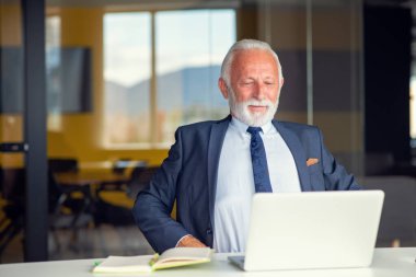 Evde dizüstü bilgisayarıyla rahat işyerinde oturan yakışıklı, gülümseyen, sosyal medyada arkadaşlarıyla sohbet eden emekli bir erkek.