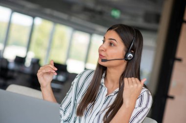 Esmer kadın dizüstü bilgisayarından arıyor kulaklık takıyor gülümsüyor ve el sallayarak web kamerasıyla iletişim kuruyor evde masada oturuyor. İnternet ve Uzaktan İletişim