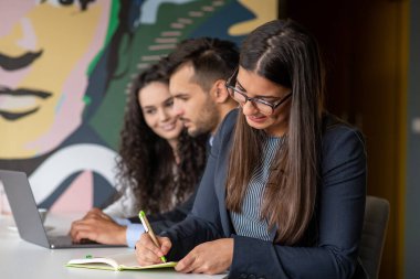 İş ekibi dizüstü bilgisayar kullanarak proje üzerinde işbirliği yapıyor. Güncel ofis ortamında sıradan iş arkadaşları birlikte çalışıyor. Takım çalışması konsepti