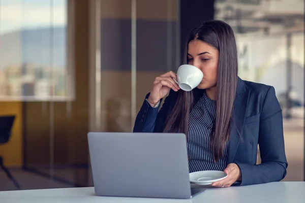 在办公室用笔记本电脑和喝咖啡的年轻女性 — 图库照片