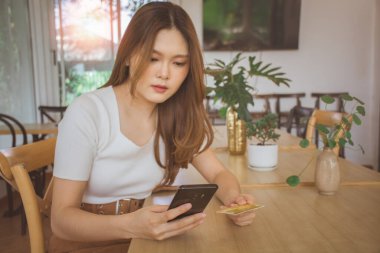 Young woman using credit card and mobile phone for online shopping in cafe, coworking space or coffee shop. Technology money wallet, online payment concept, credit card mockup. Safe mobile banking