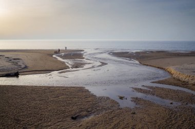 Denize doğru kumlu bir alanda kıvrılan bir nehir ile dramatik bir manzara. Bulutlu gökyüzü ile sakin ve sakin doğa sahnesi. Seyahat, doğa ya da peyzaj projeleri için mükemmel.