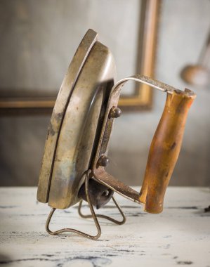 Bir tezgahın üzerine yerleştirilmiş, eski bir elektrikli ütü. Antika aletler nostalji ve ustalık hissi yayıyor..