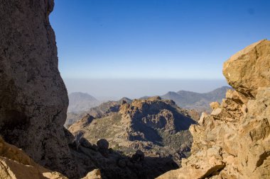 Roque Nublo, Gran Canaria 'da ikonik bir kaya oluşumu. Çam ağaçları ve açık mavi gökyüzü ile dramatik dağ manzarası. Popüler turizm merkezi. Doğa, seyahat ve peyzaj projeleri için mükemmel