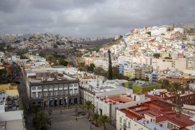 Gran Canaria, Las Palmas 'daki şehir manzarası. Mimari tarzları olan bir tepedeki binalar. Hava bulutlu. Palmiye ağaçları tropikal bir dokunuş ekler.