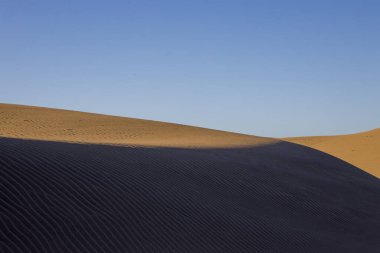 Gran Canaria 'daki Maspaloma Kumulları. Desenli kum tepecikleri, gölgeler ve soluk ayak izleri. Minimalist çöl manzarası. Doğa, seyahat ya da minimalist projeler için mükemmel.