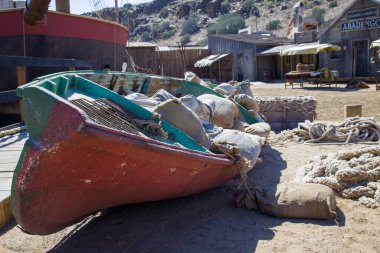 Rustic coastal scene in Gran Canaria with a small boat filled with sacks and weathered buildings. Simple living, perhaps related to fishing or local trade. clipart