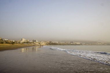 Gran Canaria 'daki Playa de Maspalomas plajı. Uzakta puslu bir şehir silueti var. Huzurlu ve huzurlu bir sahne. Plaj, seyahat, sahil ve dinlenme projeleri için mükemmel.
