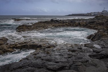 Dramatic coastal scene in Gran Canaria with waves crashing against dark volcanic rocks. Moody and powerful atmosphere. El Bufadero clipart