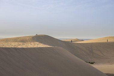 Geniş kum tepecikleri ve ölçeği vurgulayan küçük bir figür. Dalgalanan kum ve çoğunlukla açık gökyüzü olan çöl manzarası. Doğa, seyahat ve macera projeleri için mükemmel.