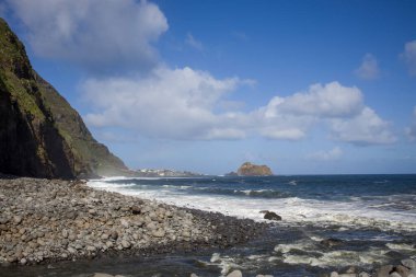 Madeira 'daki kayalık kıyı şeritlerine çarpan dalgalar, yüksek uçurumlar tarafından çerçeveleniyor. Yukarıdaki açık mavi gökyüzü bu kıyı manzarasının manzaralı güzelliğini arttırıyor..