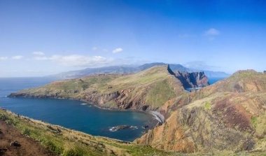 Bu nefes kesici manzara, parlak bir gökyüzü altında Madeira Ponta de Sao Lourenco 'nun dramatik uçurumlarını ve berrak mavi sularını yakalar. Yürüyüşçüler engebeli araziyi keşfederken görülebilir.