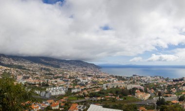 Bereketli yeşil tepeler Madeira 'da bulutlu bir gökyüzünün altında manzarayı noktalayan binalar ile pitoresk bir kasabayı çevrelemektedir. Doğa ve mimari bu canlı yerde kusursuz bir şekilde harmanlanır..