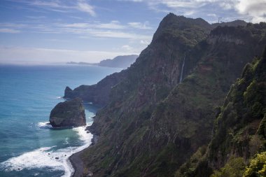 Bu nefes kesici manzara, Madeira 'nın turkuaz okyanustan yükselen dramatik uçurumlarını yakalar. Dalgalar açık bir gökyüzünün altında kayalık kıyı şeridine çarpar ve barışçıl bir ortam yaratır..