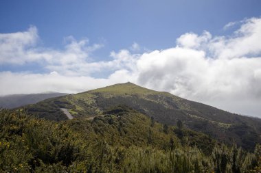 Canlı yeşillik Madeira 'nın yamaçlarını kaplıyor ve adanın doğal güzelliğini gözler önüne seriyor. Bulutlar mavi gökyüzünde sürükleniyor, dingin manzaraya derinlik katıyor..
